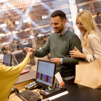 Young couple paying female sales assistant with credit card in c